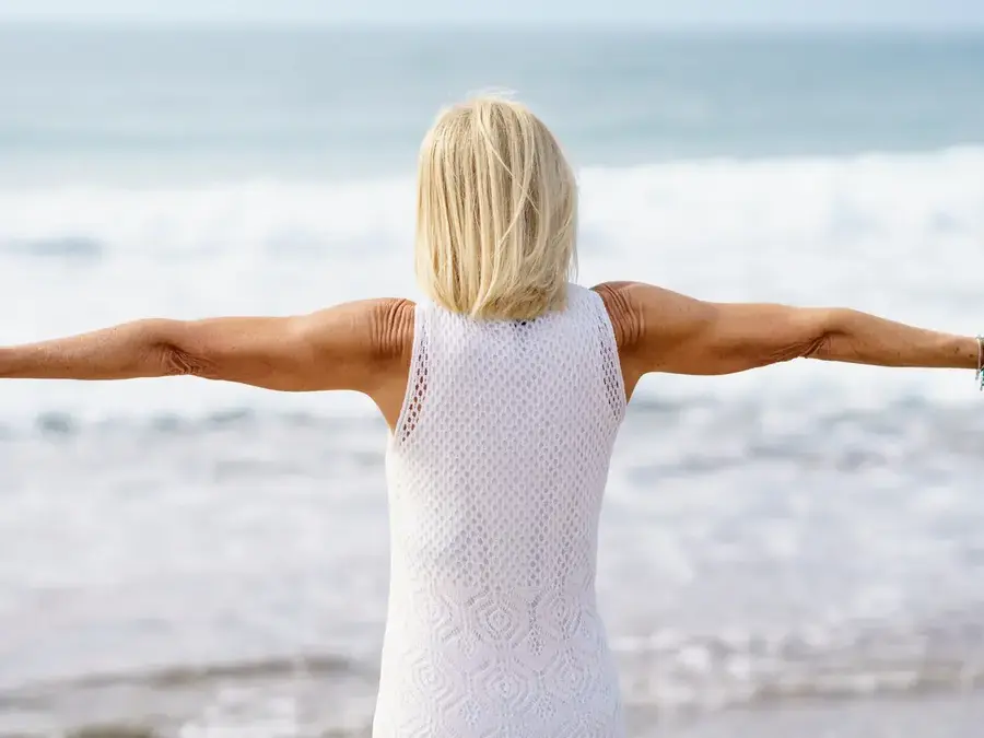Stock photo: woman in a white summer dress with open arms by the sea